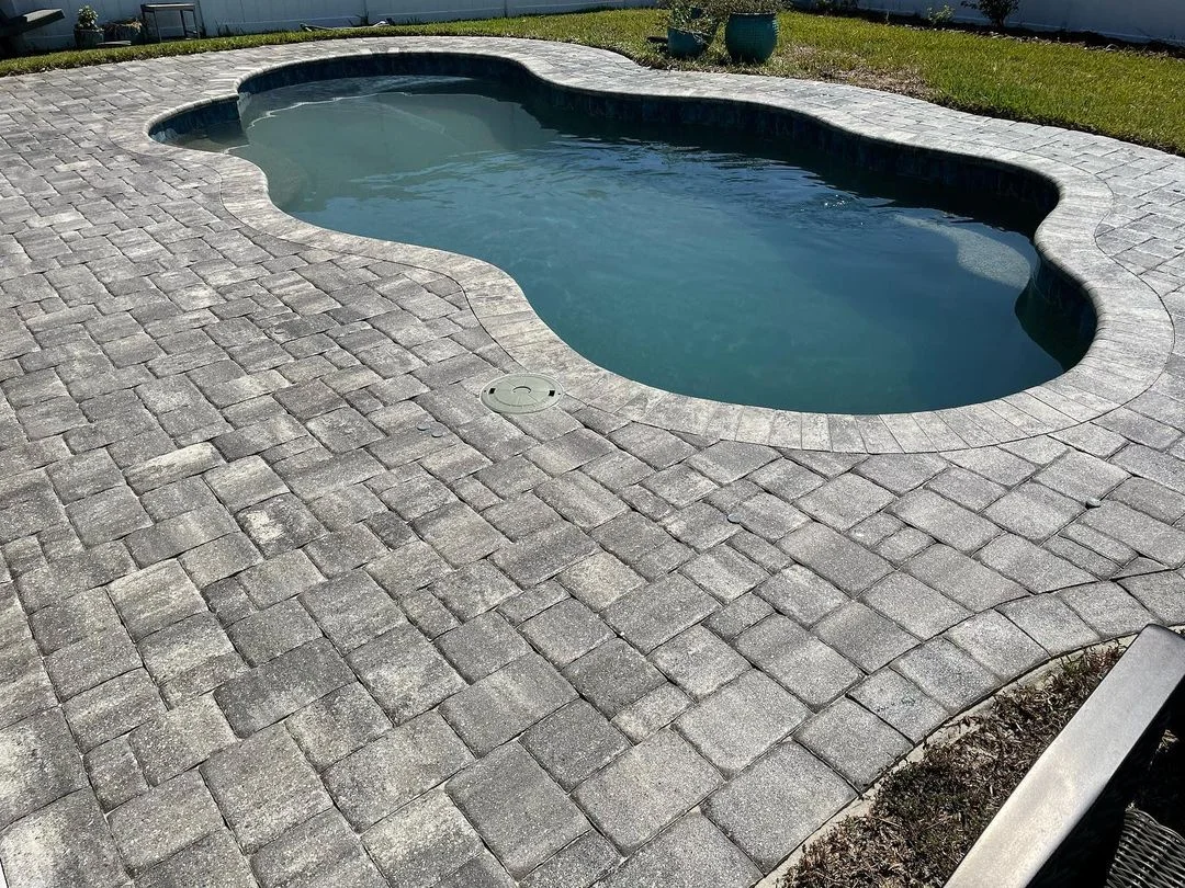 Gray concrete pavers sealed in herringbone pattern around pool deck