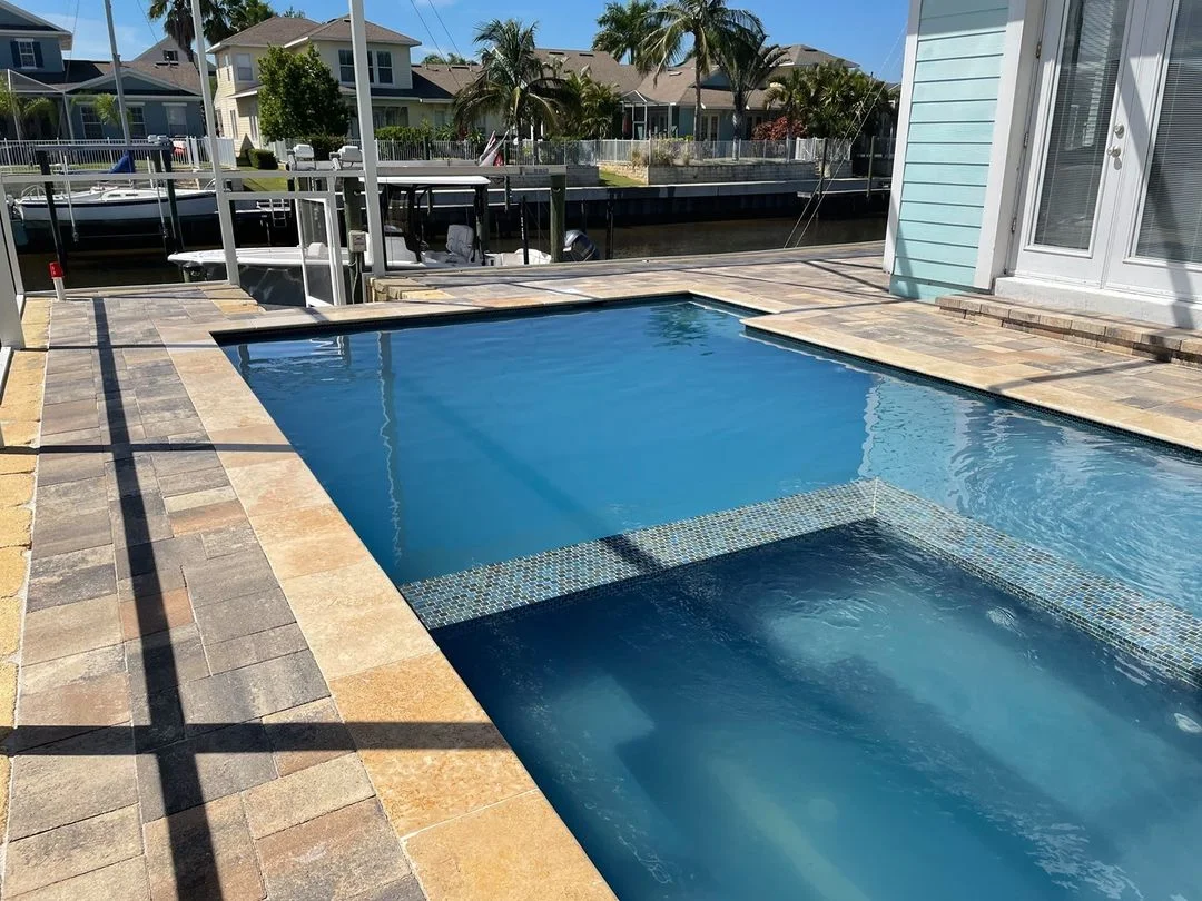 Sealed travertine pool deck with geometric paver pattern, spa, and waterfront dock